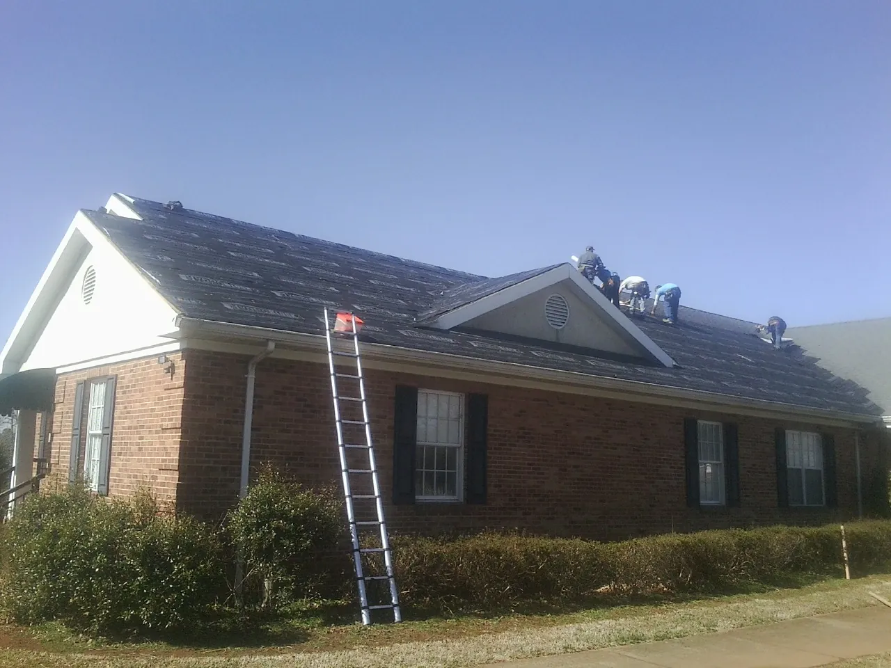 Crew tearing shingles off a brick ranch roof with a ladder set — Metal Roof Repair work by our crew in Montesano