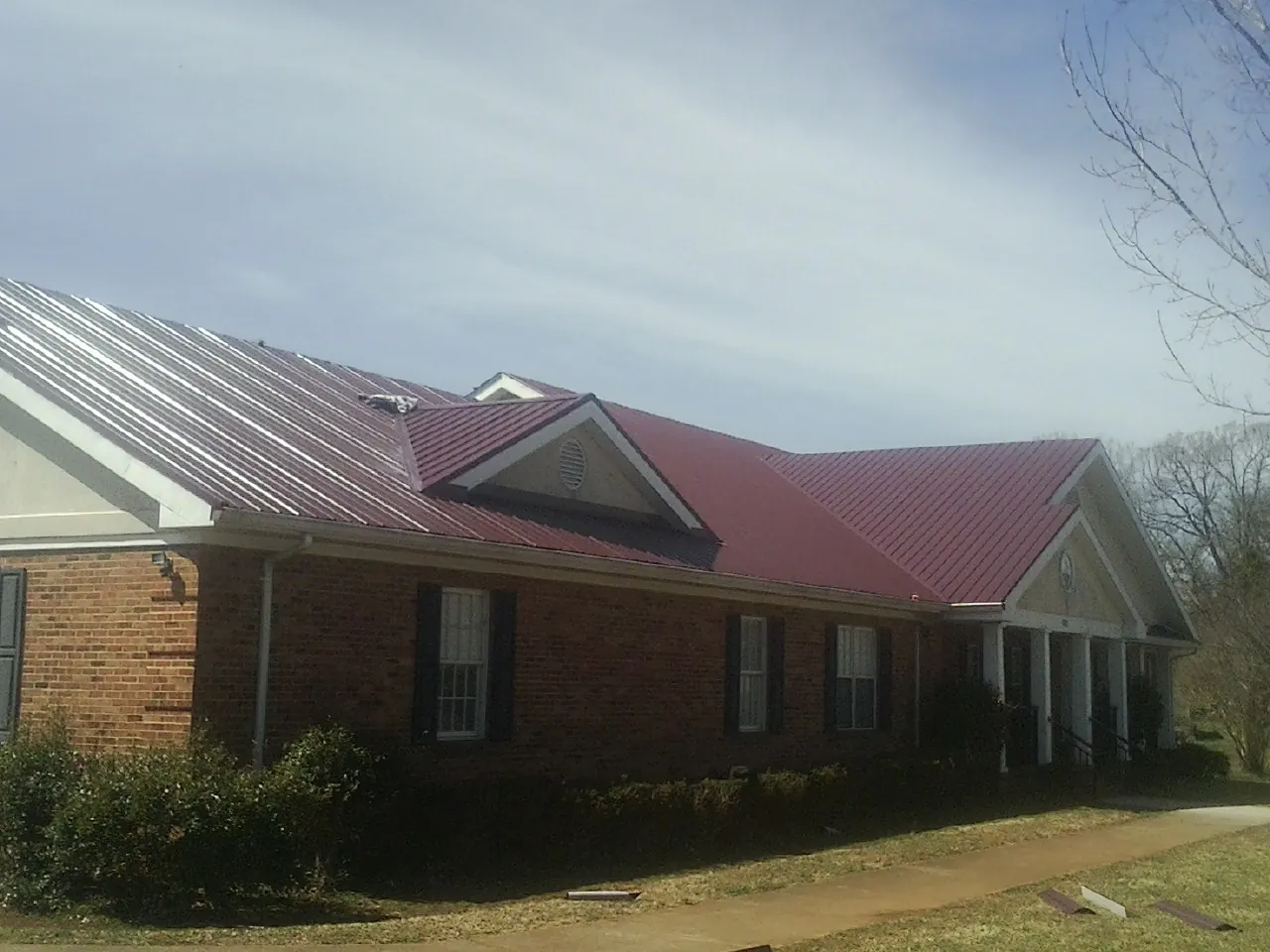 Red metal roof with gabled entries on a long brick building, from a Hail Damage Roof Repair job in Montesano