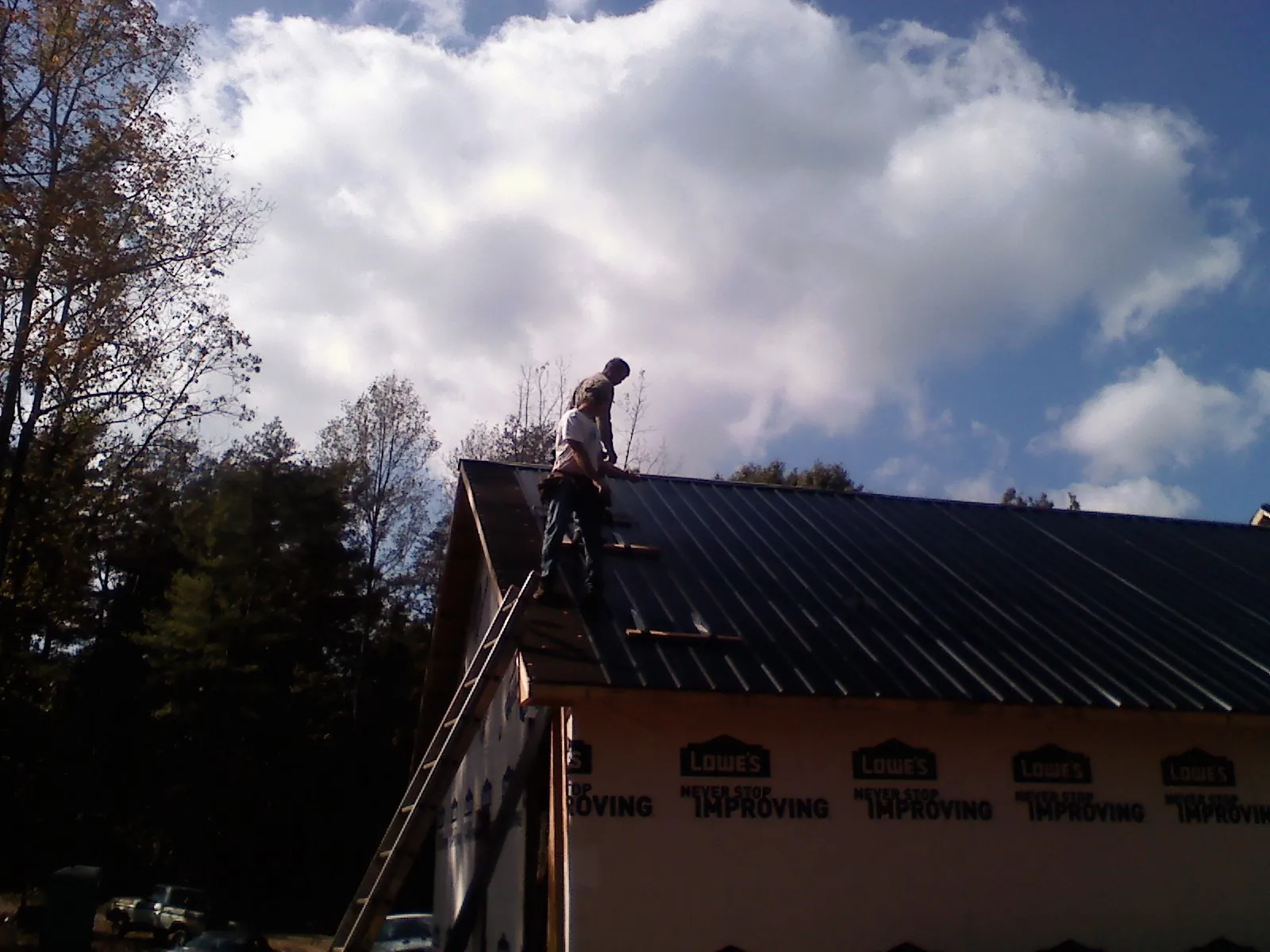 Roofer fastening dark metal panels high against a cloudy sky, from a Roof Inspection job in Montesano
