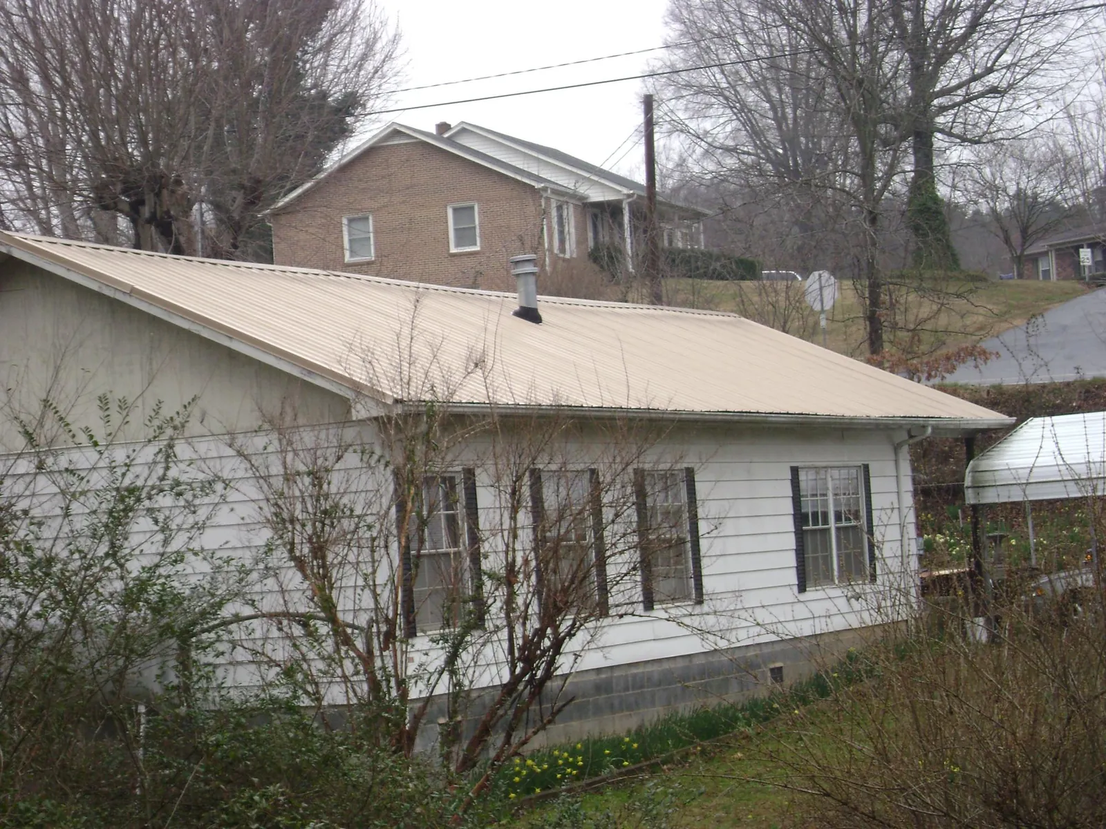 Tan metal roof on a white sided house set into a hillside — Commercial Roofing by Roofing Brothers in Montesano